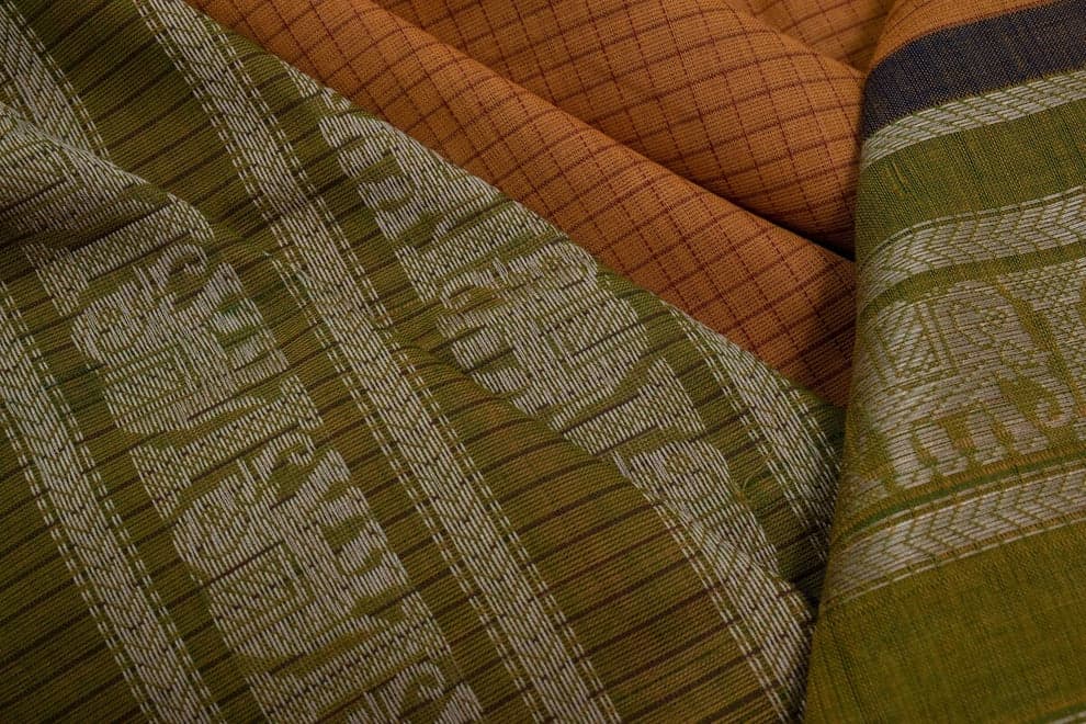 Folds of handloom cotton showing woven motifs in green, silver, and rust